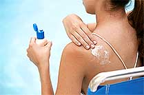 A woman applies sunscreen to her shoulder.